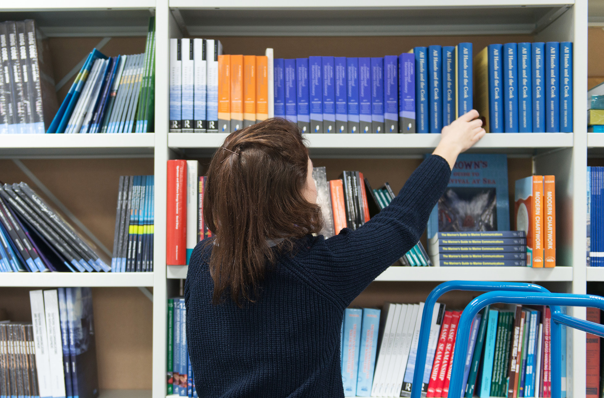 A woman picking out a book from the library shelf